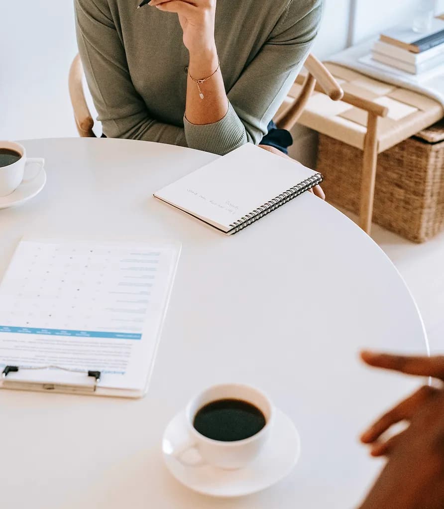 Hands reviewing documents at a table with a notebook and coffee
